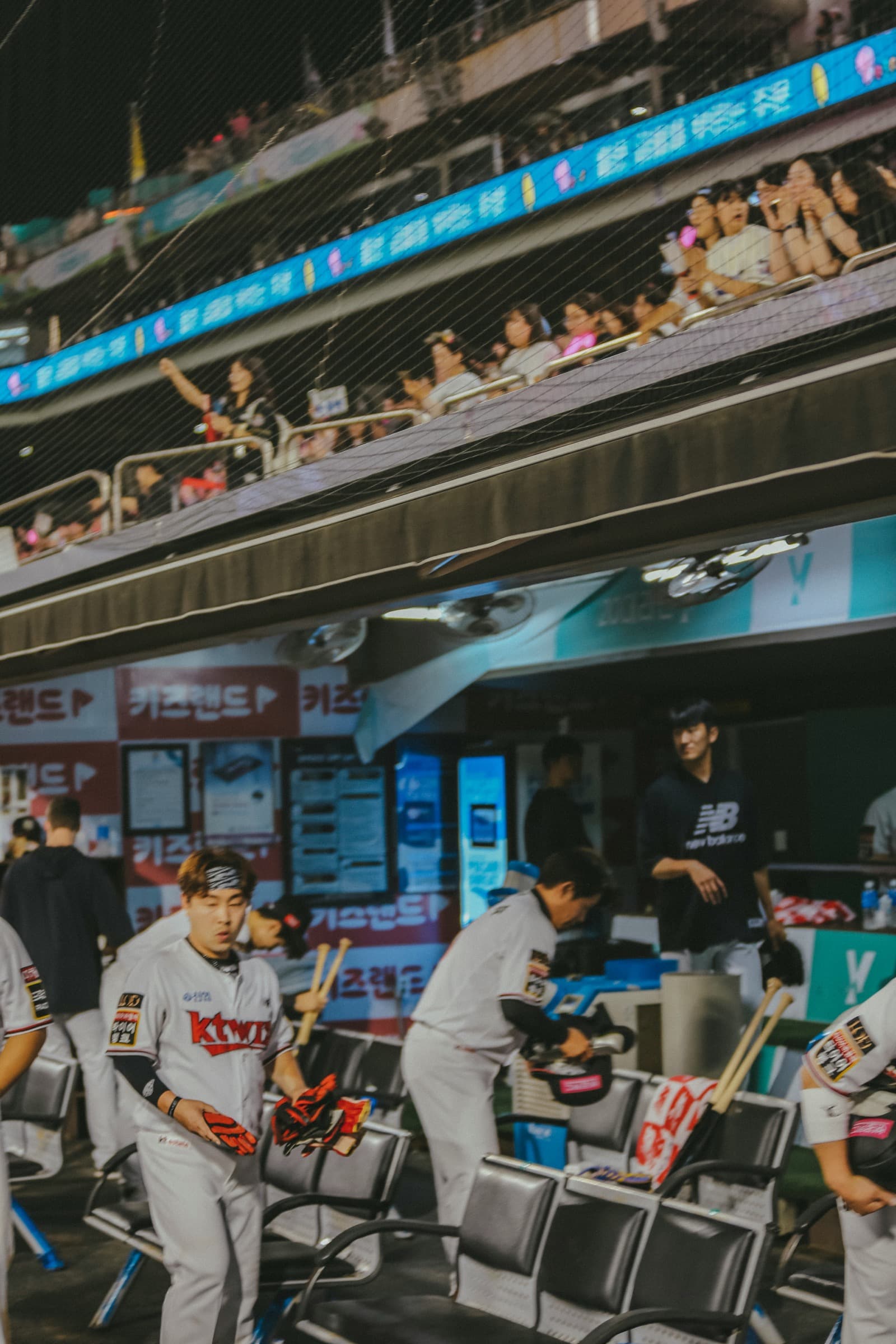 Players and staff in a dugout during a night game.