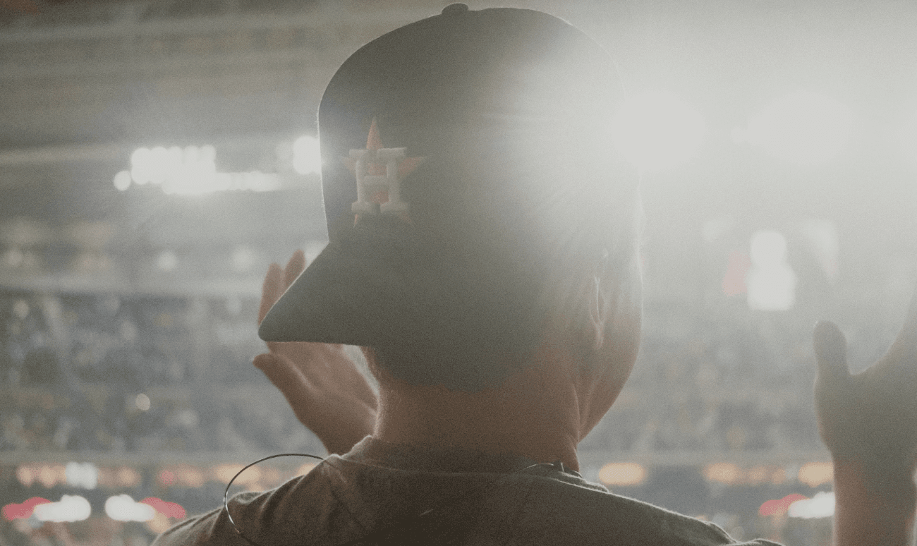 A figure in a ballcap standing in a stadium, lit from the field.