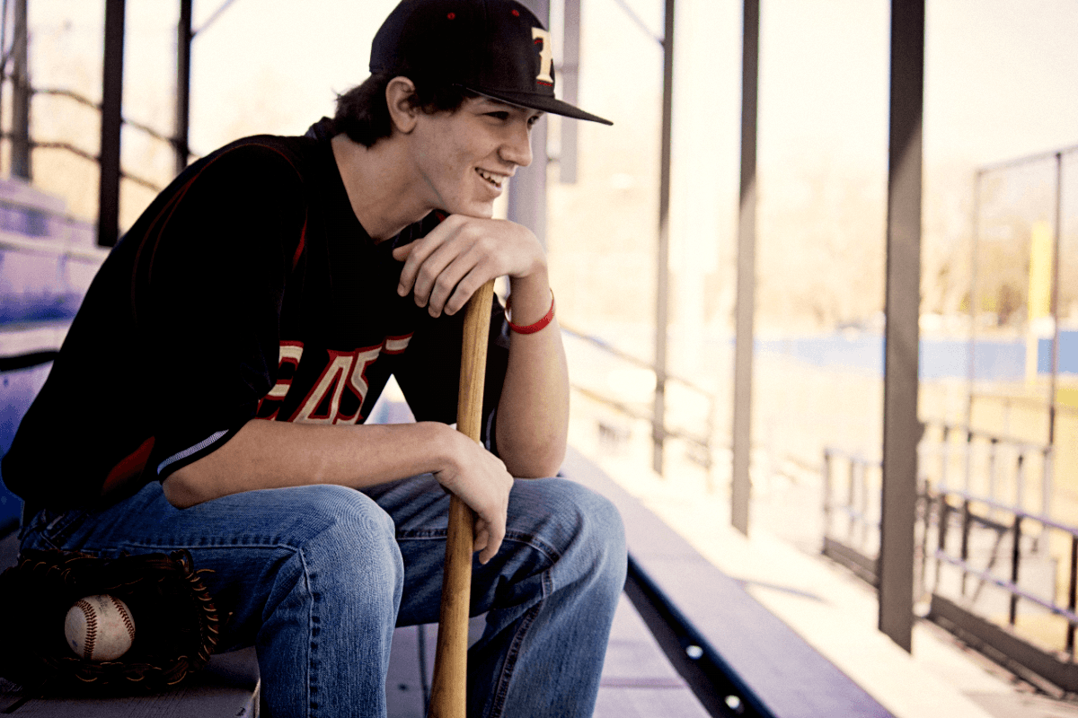 A player sitting in the bleachers with a bat and glove.