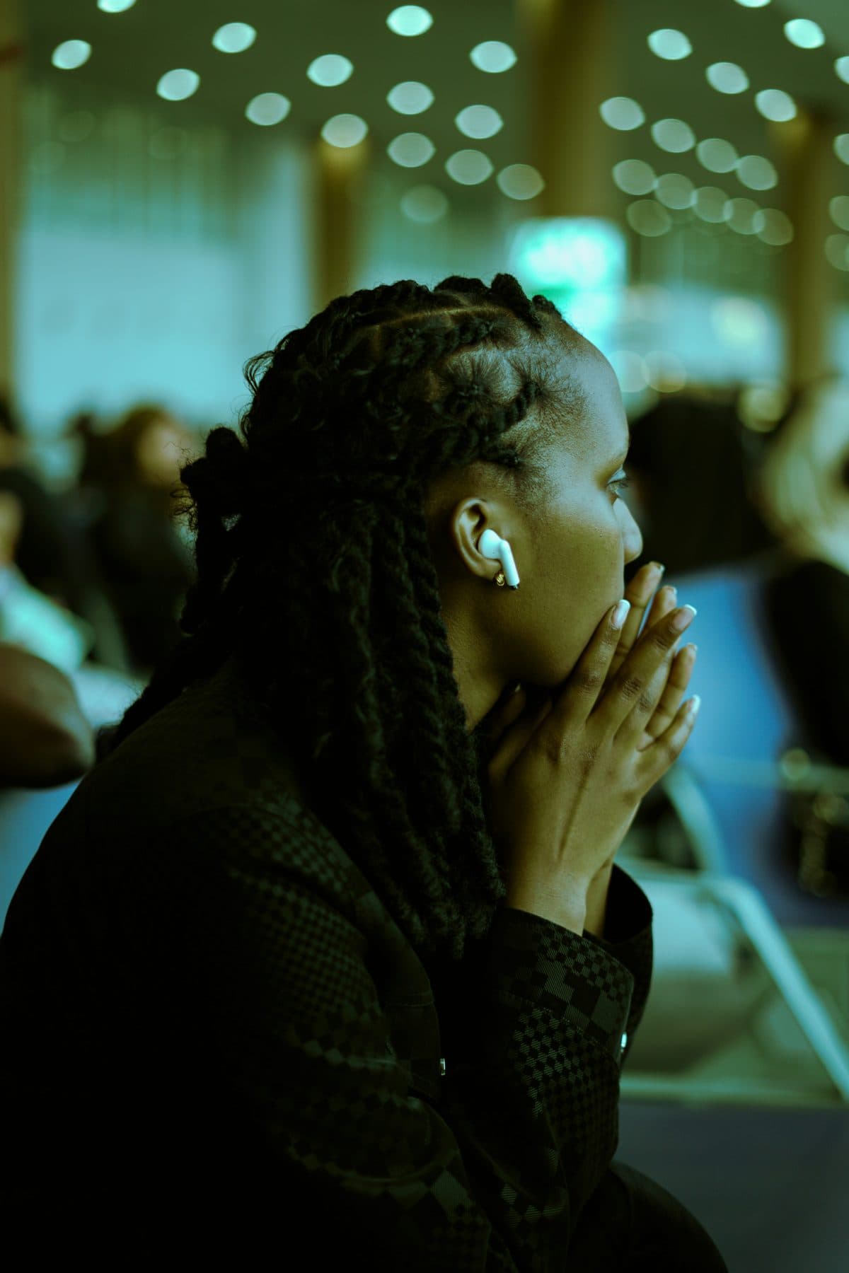 A woman listening through an earbud, hands folded, in a quiet moment during a gathering.