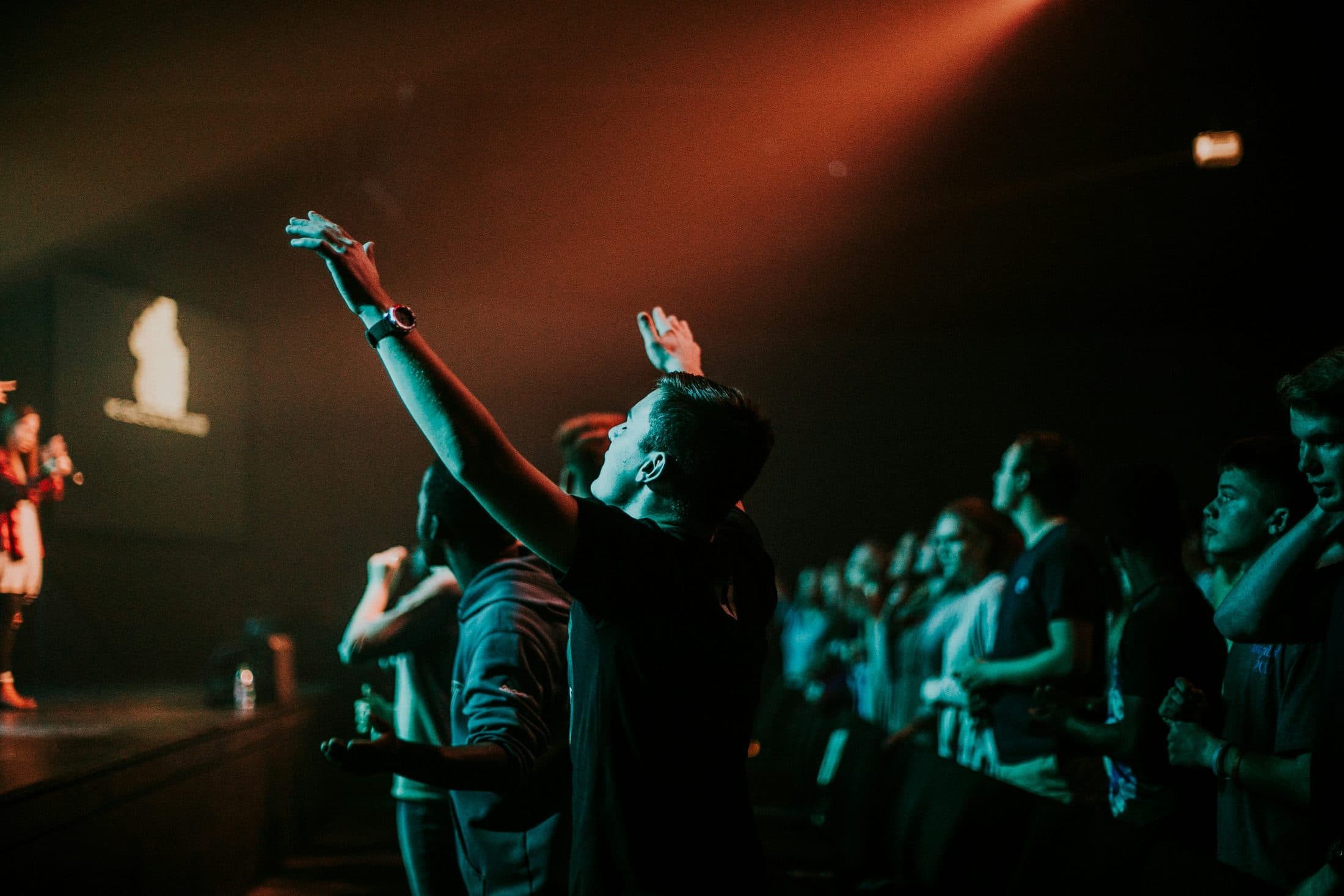 A congregation standing together with hands raised during a worship gathering.