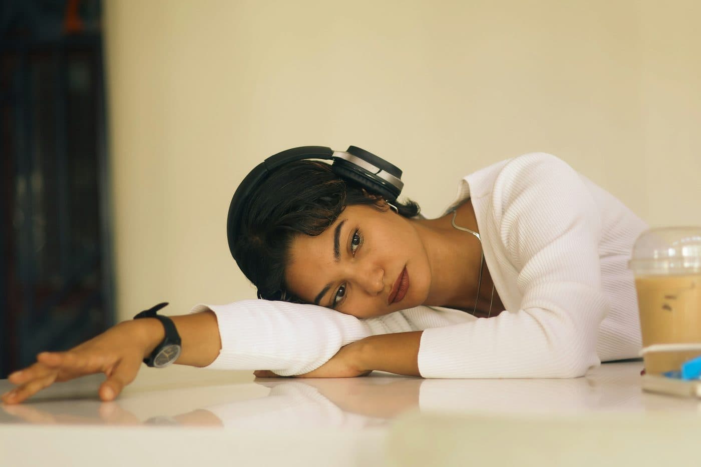 A woman resting her head on a table, listening through over-ear headphones.